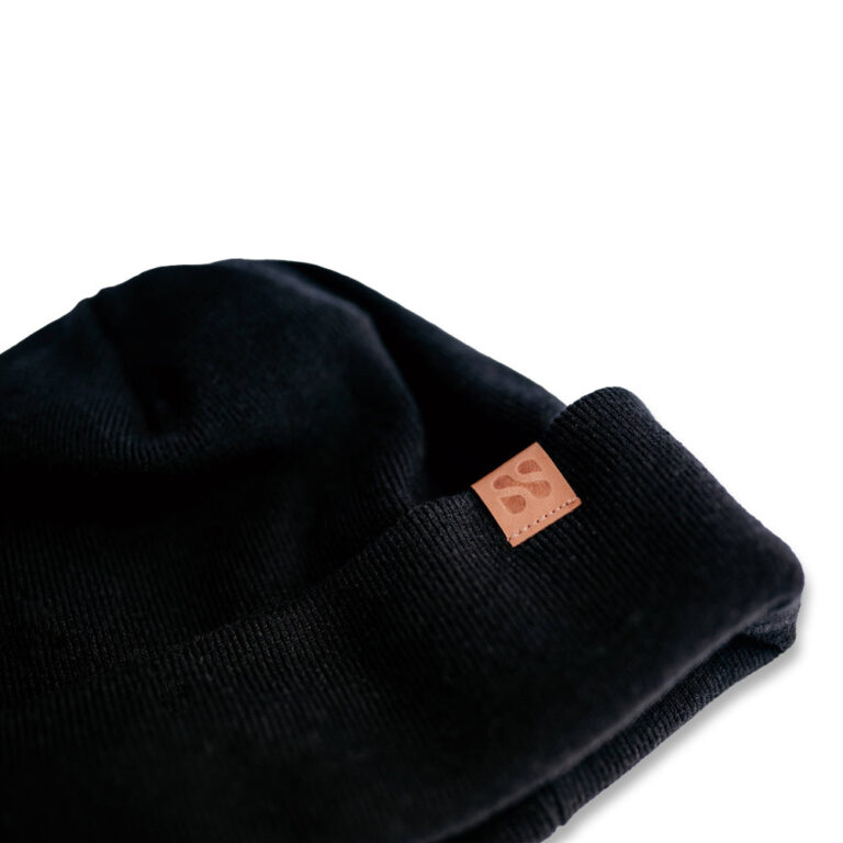 Black knit beanie with brown leather logo patch, neatly folded on white background