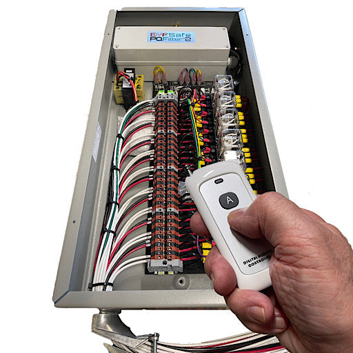 Hand holding white remote near open electrical panel with colorful wired circuit breakers in metal enclosure