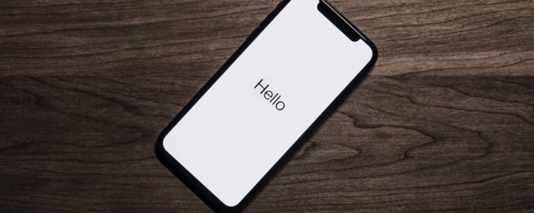 iPhone with "Hello" displayed on white screen, lying on wooden surface with grain texture