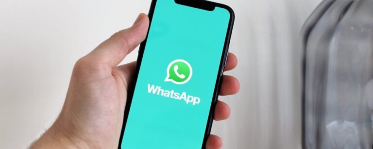 Hand holding smartphone with WhatsApp logo on teal screen against blurred background